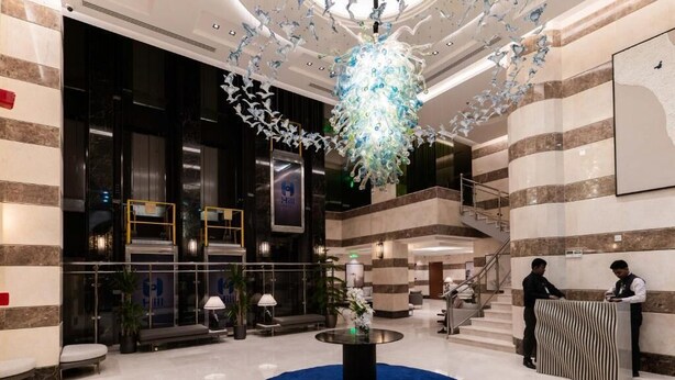 A modern hotel lobby with a central round table, a reception desk, and a staircase leading to upper floors. - Hill Hotel (Madinah)