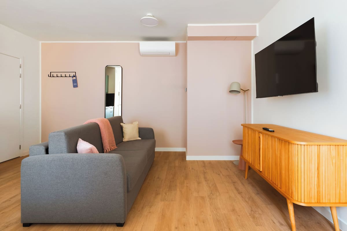 Un salon moderne avec un canapé gris, un buffet en bois et un téléviseur à écran plat fixé au mur.