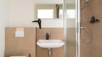A modern bathroom with a glass shower enclosure, a white sink, and a hairdryer mounted on the wall.