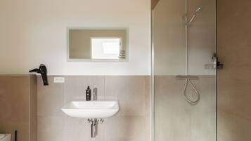 Un baño moderno con lavamanos, espejo y ducha.