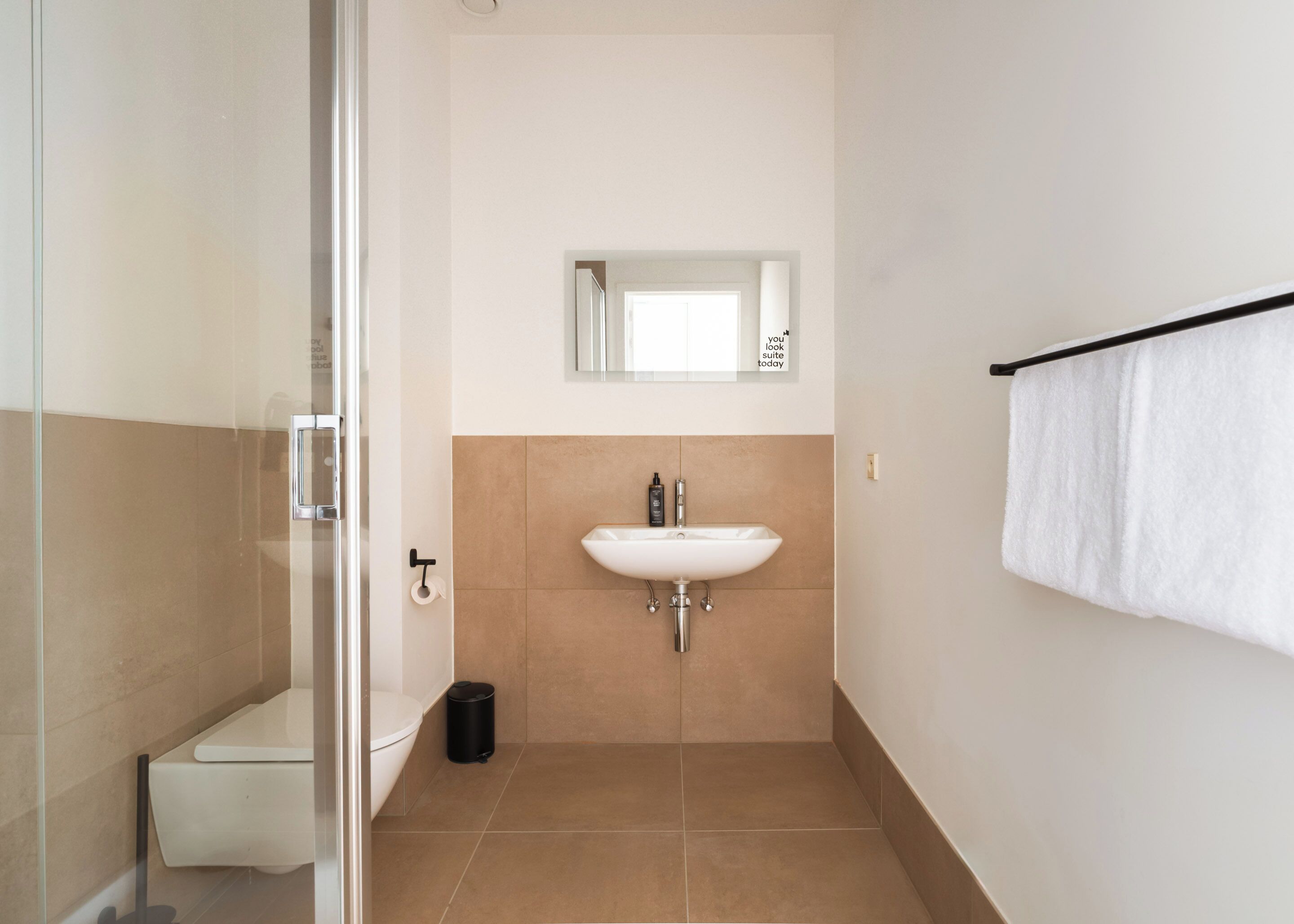 Un bagno con cabina doccia in vetro, un lavandino bianco e un portascopevoli.
