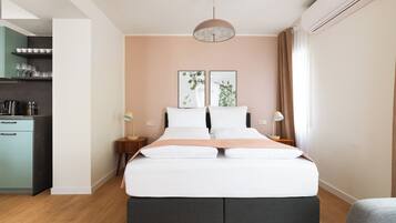 A modern bedroom with a bed, bedside tables, a hanging light fixture, and a view of the kitchen area.