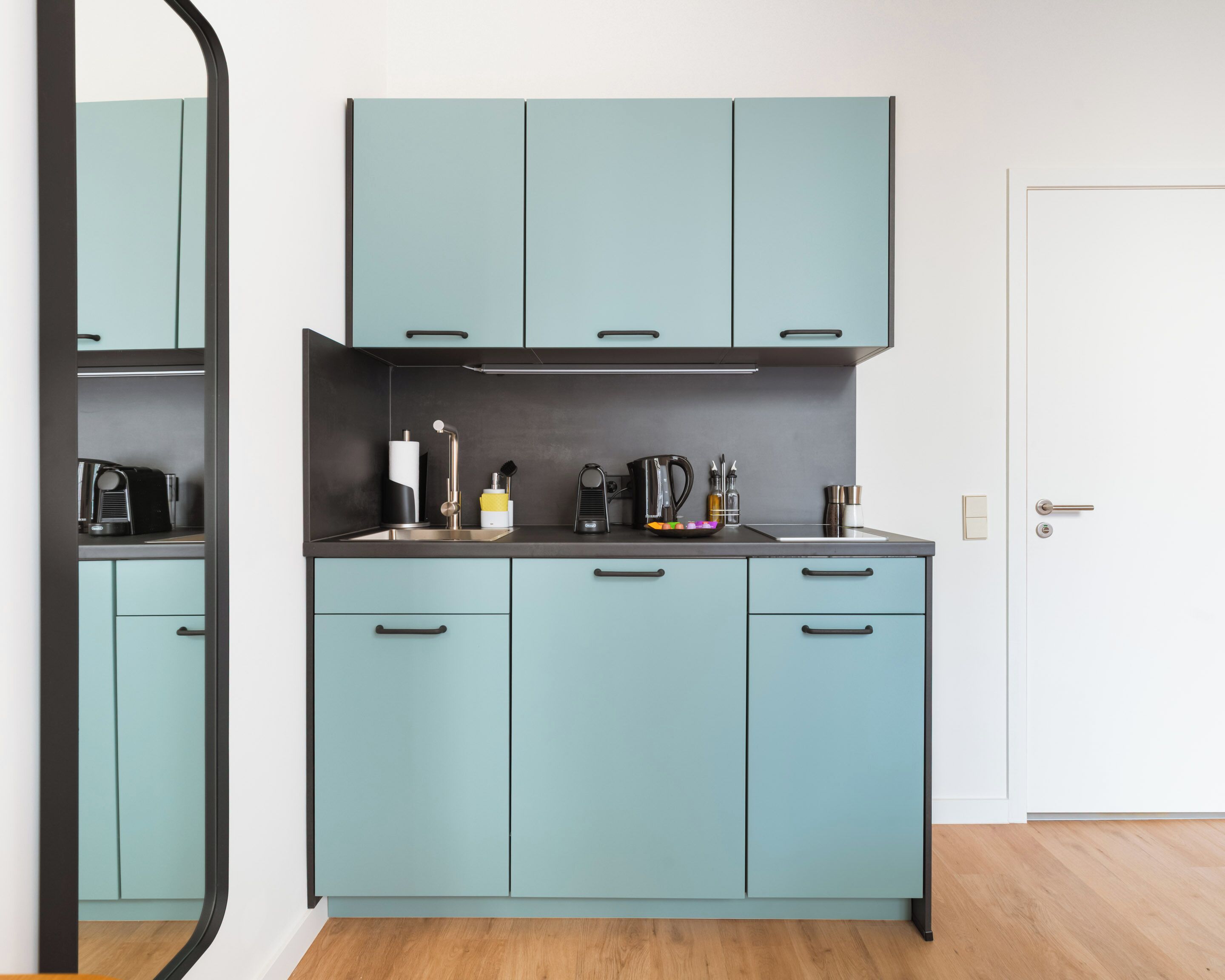 A compact kitchen with light blue cabinets, a stainless steel sink, and modern appliances.