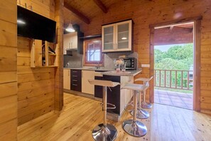 A wooden cabin interior with a kitchen, bar stools, and a view of the outdoors.
