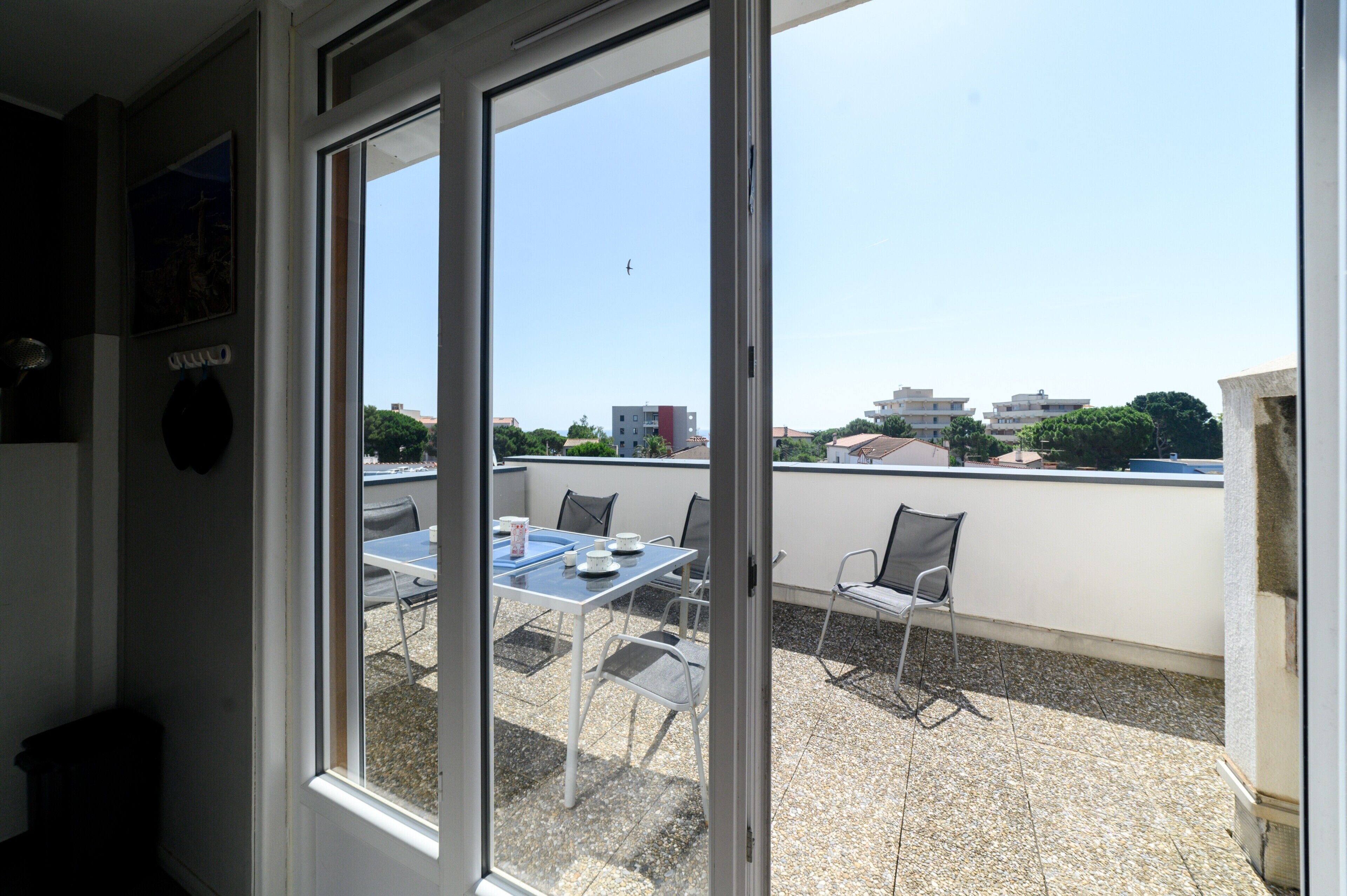 Un balcon avec une table et des chaises, une vue dégagée sur les bâtiments au loin et une porte donnant sur l’intérieur.