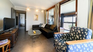 A living room with a sofa, a coffee table, a TV, and a window with curtains. - Apartment 'Appartemen' with Sea View, Balcony and Wi-Fi (Argelès-Plage)