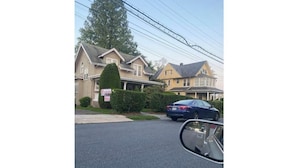 A residential street with houses, a car parked on the side, and a 'For Sale' sign.
