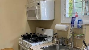 A compact kitchen with white cabinets, a stove, a microwave, and a sink.