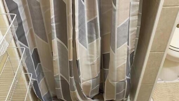 A shower area with a patterned shower curtain, a black textured mat, and a metal shelf.