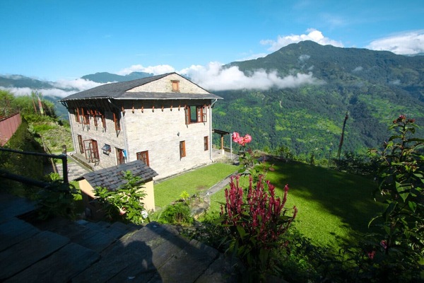 Mountain villa surrounded by lush hills and Himalayan peaks.