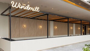 A modern hotel reception area with a wooden panel wall, a white reception desk, and a neon sign reading "The Windmill". - Hotel Golden Tulip Essential PIK2 Jakarta (Teluknaga)