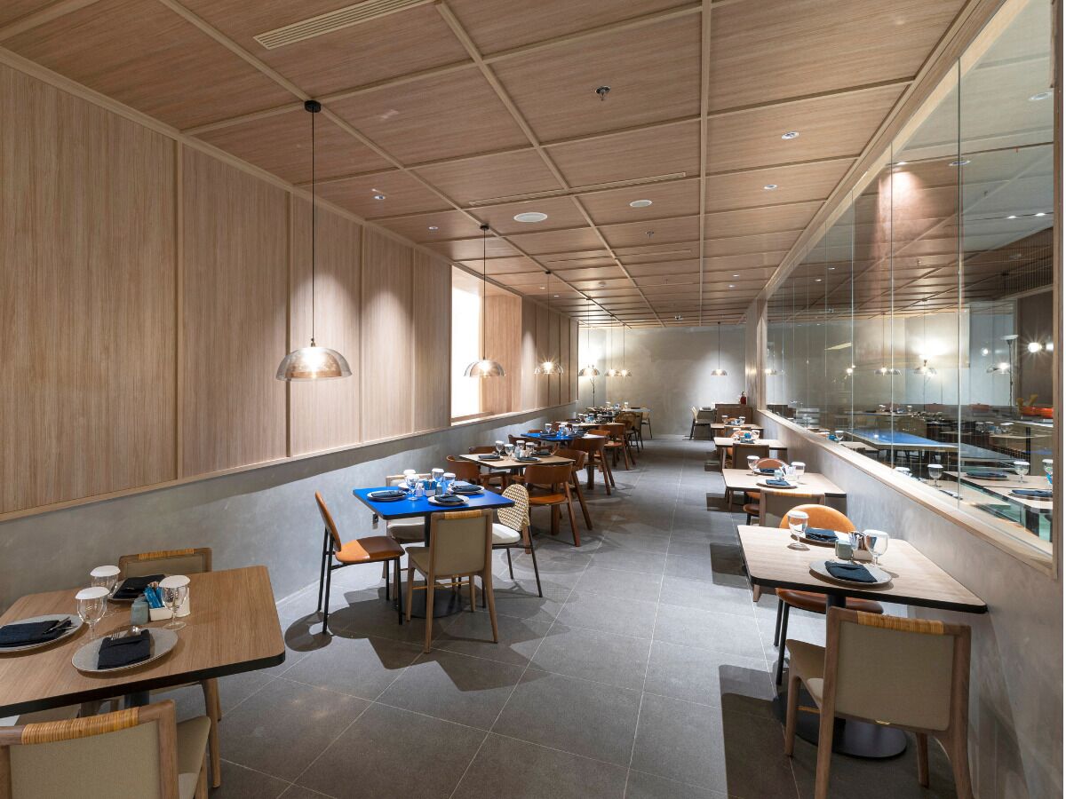 A modern restaurant with wooden panel walls, long communal tables, and pendant lighting.
