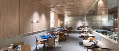 A modern restaurant with wooden panel walls, long communal tables, and pendant lighting.