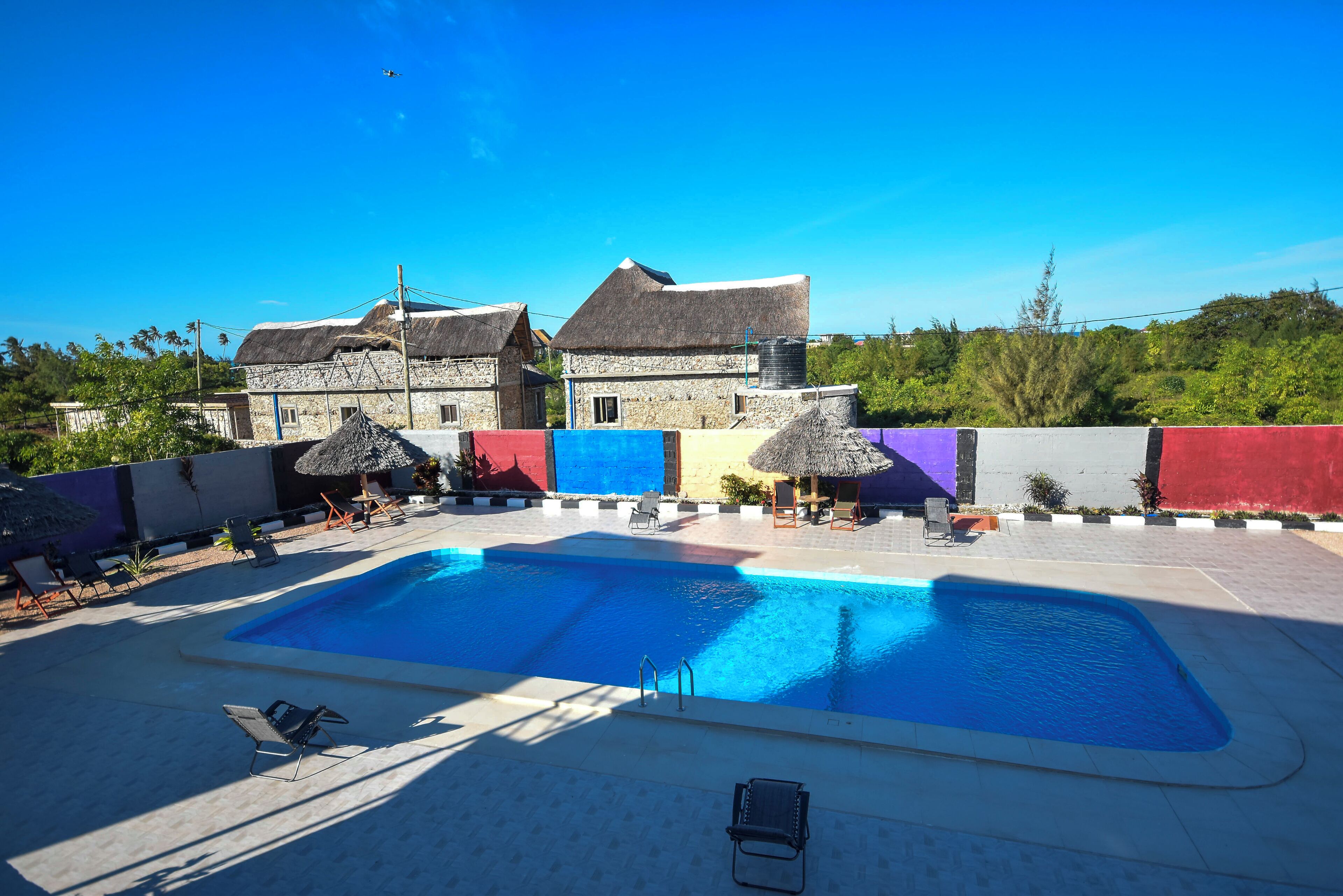 A swimming pool with lounge chairs and umbrellas, surrounded by a stone building with a thatched roof.