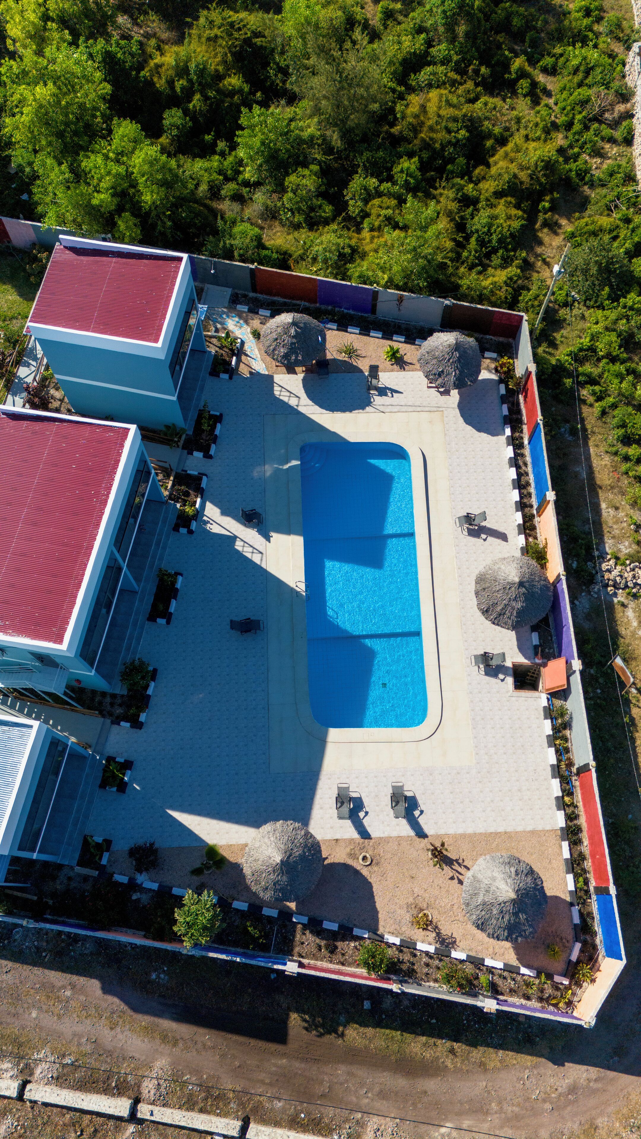 An aerial view of a resort with a swimming pool, lounge chairs, and a red-roofed building.
