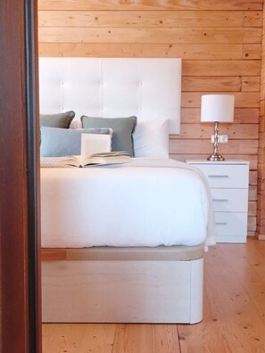 A bedroom with a large bed, a bedside table with a lamp, and a wooden wall.