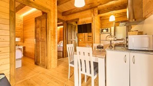 A wooden cabin interior with a dining area, kitchen, and a bed visible through an open door. - Cottage : Nature + comfort 5' from the beach (Bueu)