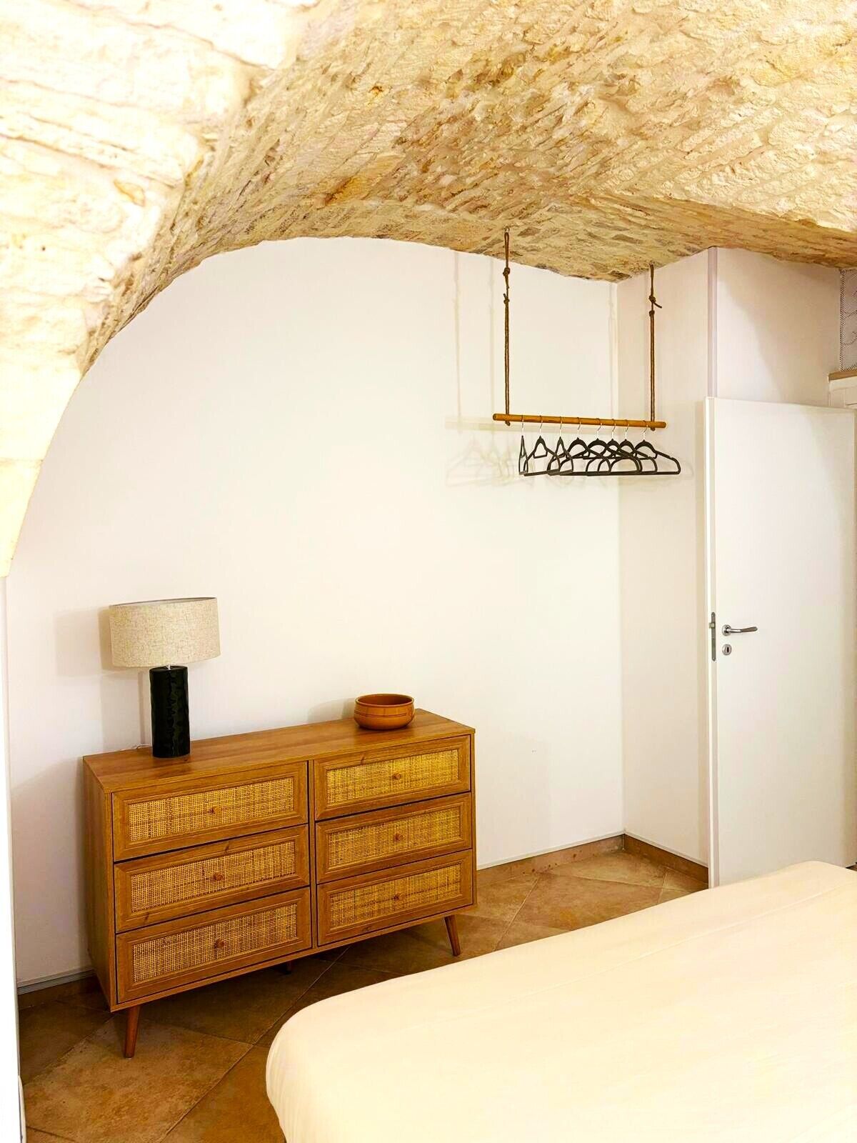 A bedroom with a bed, a wooden dresser, a hanging clothes rack, and a door.