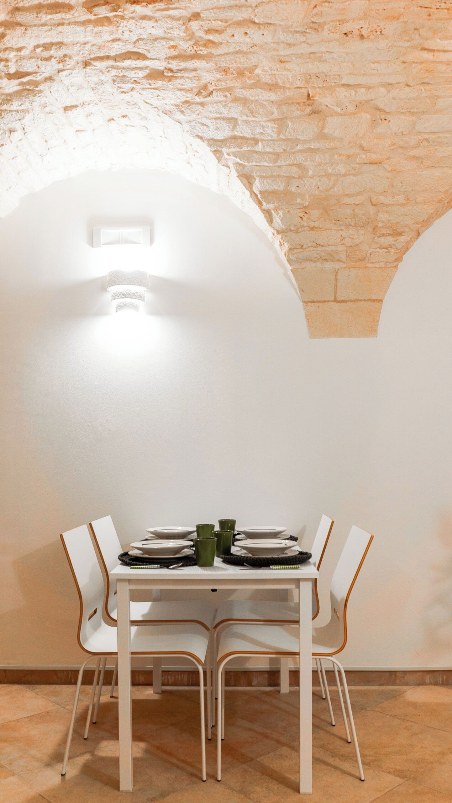 A dining area with a white table set for four, surrounded by white chairs with wooden accents.