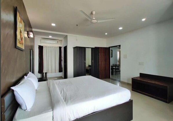 A modern hotel room with a large bed, a desk, a wardrobe, and a ceiling fan. - Seaface Properties (Daman)