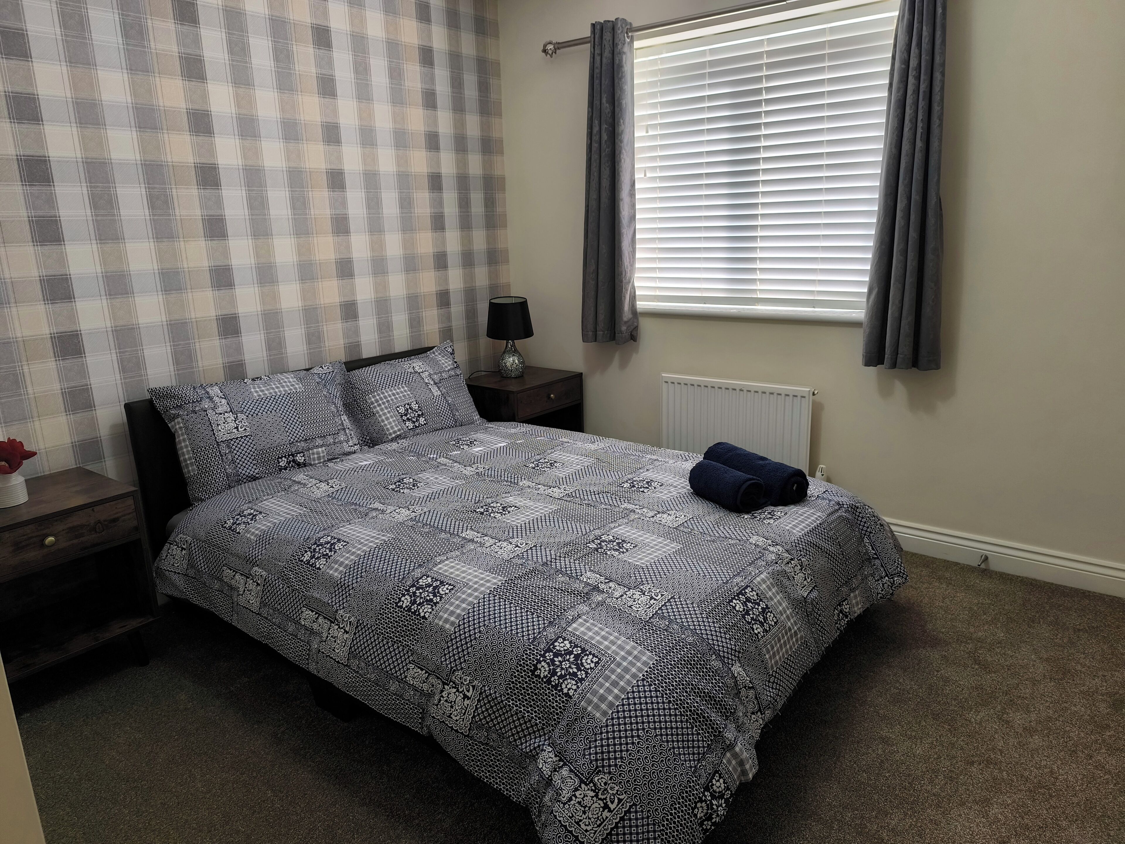A bedroom with a bed, a nightstand, a lamp, a radiator, and a window with curtains.