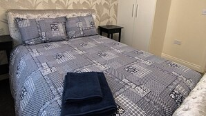 A bedroom with a patterned bedspread, a neatly folded dark blue towel, a headboard, and a wardrobe. - Cozy Corner For You ! (Newcastle-upon-Tyne)