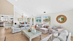 A spacious living room with a large glass coffee table, multiple seating areas, and a view of the outdoors through large windows. - Entire Villa Nature View-Heated Pool/Block to Sand (Fort Myers Beach)