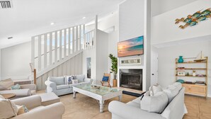 A spacious living room with a high ceiling, a fireplace, and a staircase leading to an upper level. - Entire Villa Nature View-Heated Pool/Block to Sand (Fort Myers Beach)
