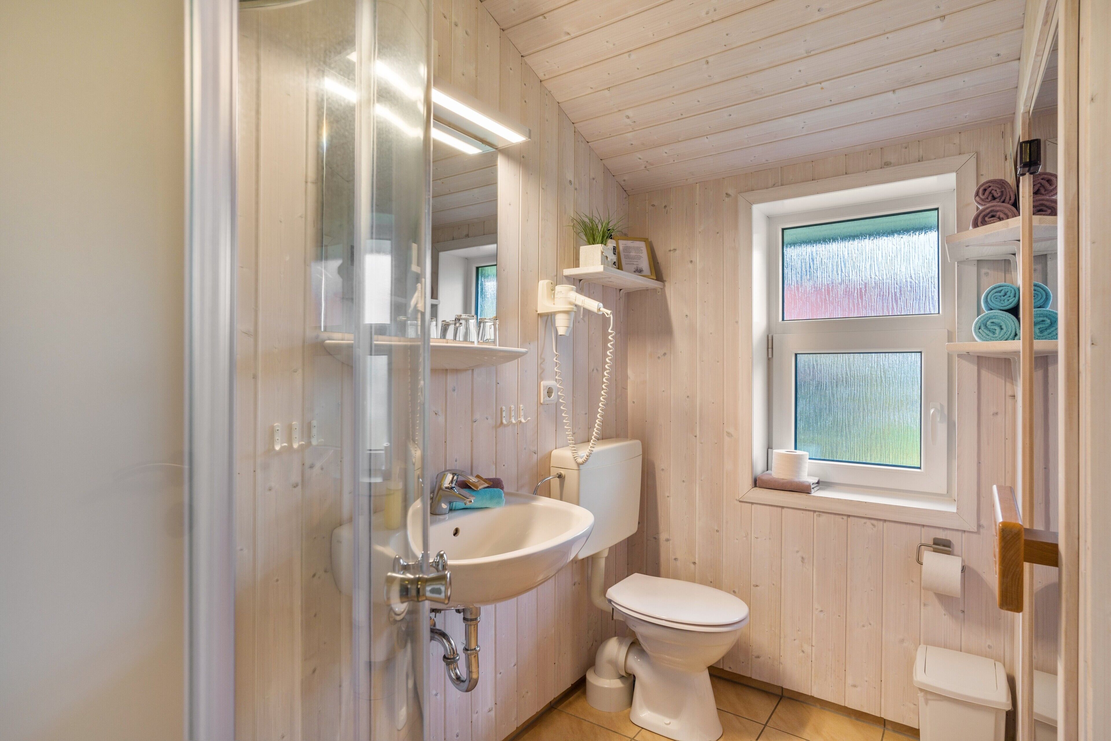 Une salle de bain avec un intérieur en bois, un lavabo blanc, des toilettes et une fenêtre donnant sur un beau paysage.