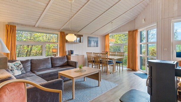 A cozy living area with a sofa, dining table, chairs, and a fireplace. - Holiday Home 'Skipper-Lodge West' with Sea View, Private Terrace and Wi-Fi (Kosel)