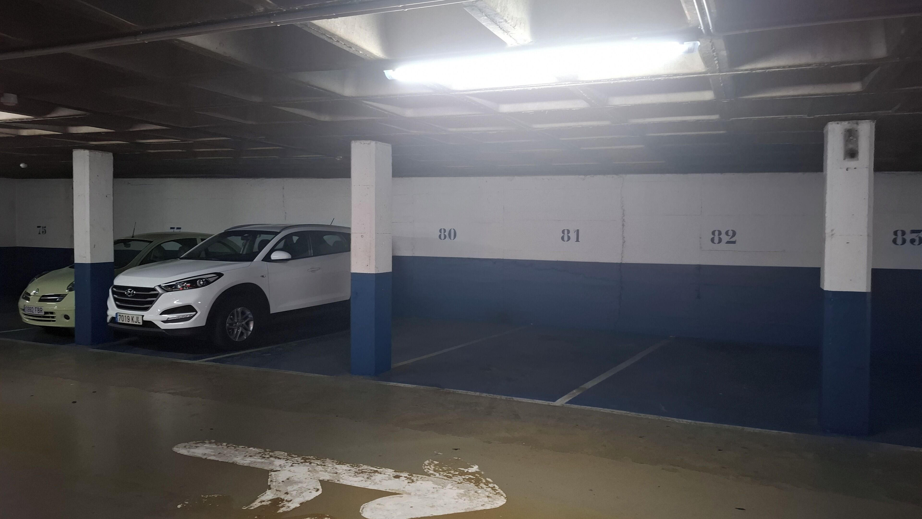 Un estacionamiento con espacios numerados, un coche blanco estacionado en el espacio 80 y otro coche blanco en el espacio 82.