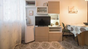 A compact living space with a television, a small refrigerator, a dining table with chairs, and a patterned floor.