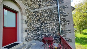 A stone building with a red door and a small outdoor seating area with metal chairs.