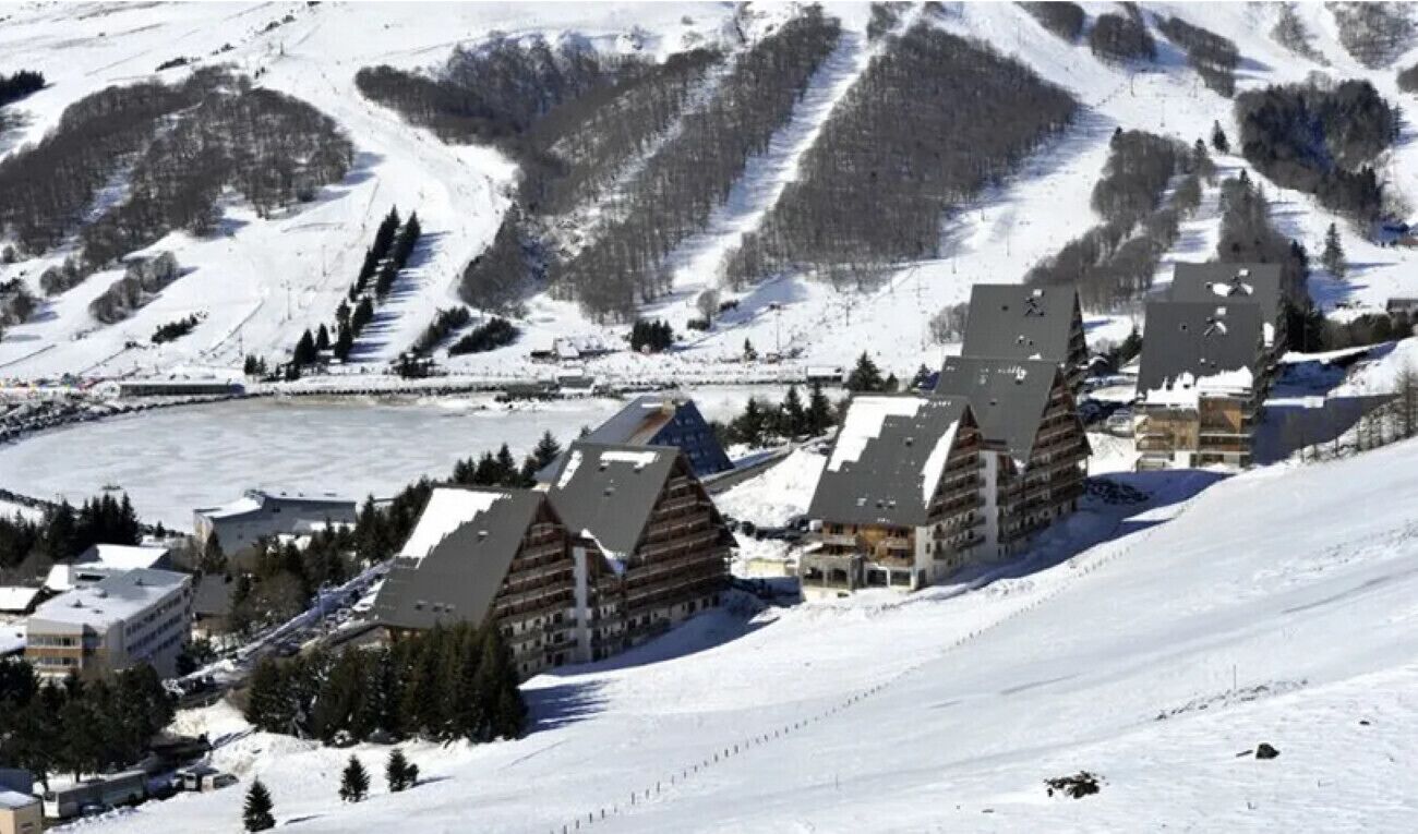 A snow-covered mountain resort with chalet-style buildings, ski slopes, and a lake.