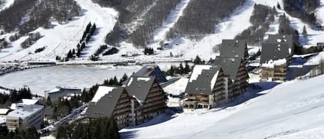A snow-covered mountain resort with chalet-style buildings, ski slopes, and a lake.