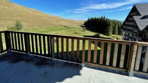 Un balcon doté d’une balustrade en bois, qui offre une vue sur une colline verdoyante et un bâtiment dont le toit est en pente.