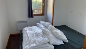 Une petite chambre avec un lit simple, une fenêtre, un radiateur et une porte en bois.