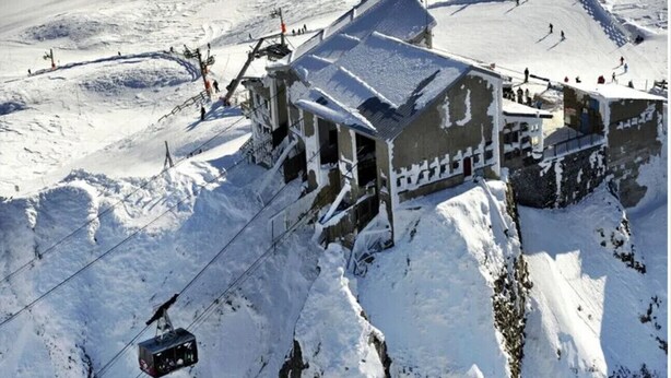 Un bâtiment enneigé avec un câble de télésiège, probablement un chalet de montagne ou une station de ski.