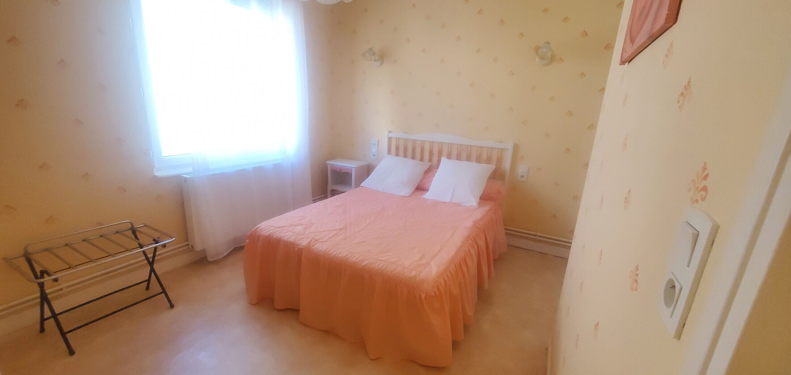 A bedroom with a bed, a nightstand, a window with curtains, and a wall-mounted light fixture.