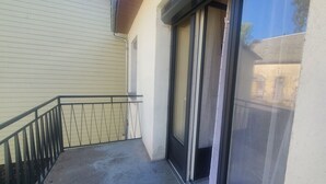 A balcony with a metal railing, a sliding glass door, and a view of a building in the background. - quietude (Murol)