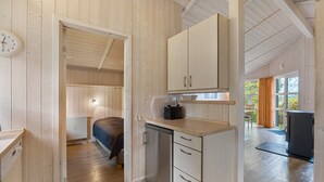 Ein kompaktes Zimmer mit einem Bett, einer kleinen Küchenzeile und einem Fenster mit Vorhängen.