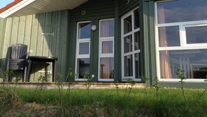 Ein grünes Gebäude mit rotem Dach, großen Fenstern und einer kleinen Terrasse mit einem Stuhl.
