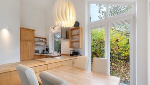Uma cozinha moderna com armários de madeira, uma mesa de jantar e uma janela grande com vista para árvores.