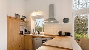 A modern kitchen with wooden cabinets, a dishwasher, an oven, a microwave, and a large window providing a view of trees.