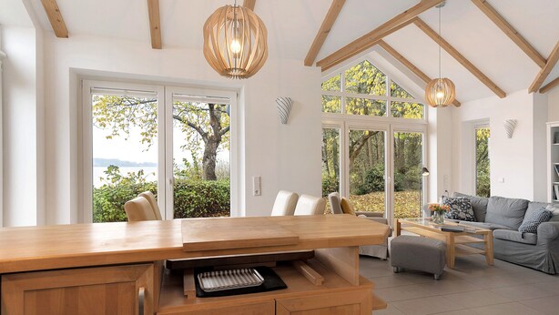 A modern kitchen with wooden cabinetry, a central island, and a dining area with a grey sofa and coffee table.