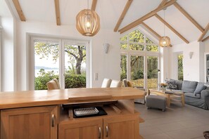Een moderne keuken met houten kasten, een centraal eiland en een zithoek met een grijze bank en salontafel.