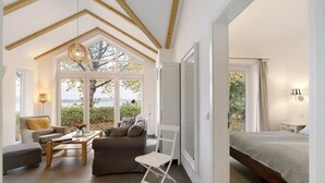 A spacious room with a bed, a sofa, a chair, and a table. There is a large window providing a view of the outdoors.