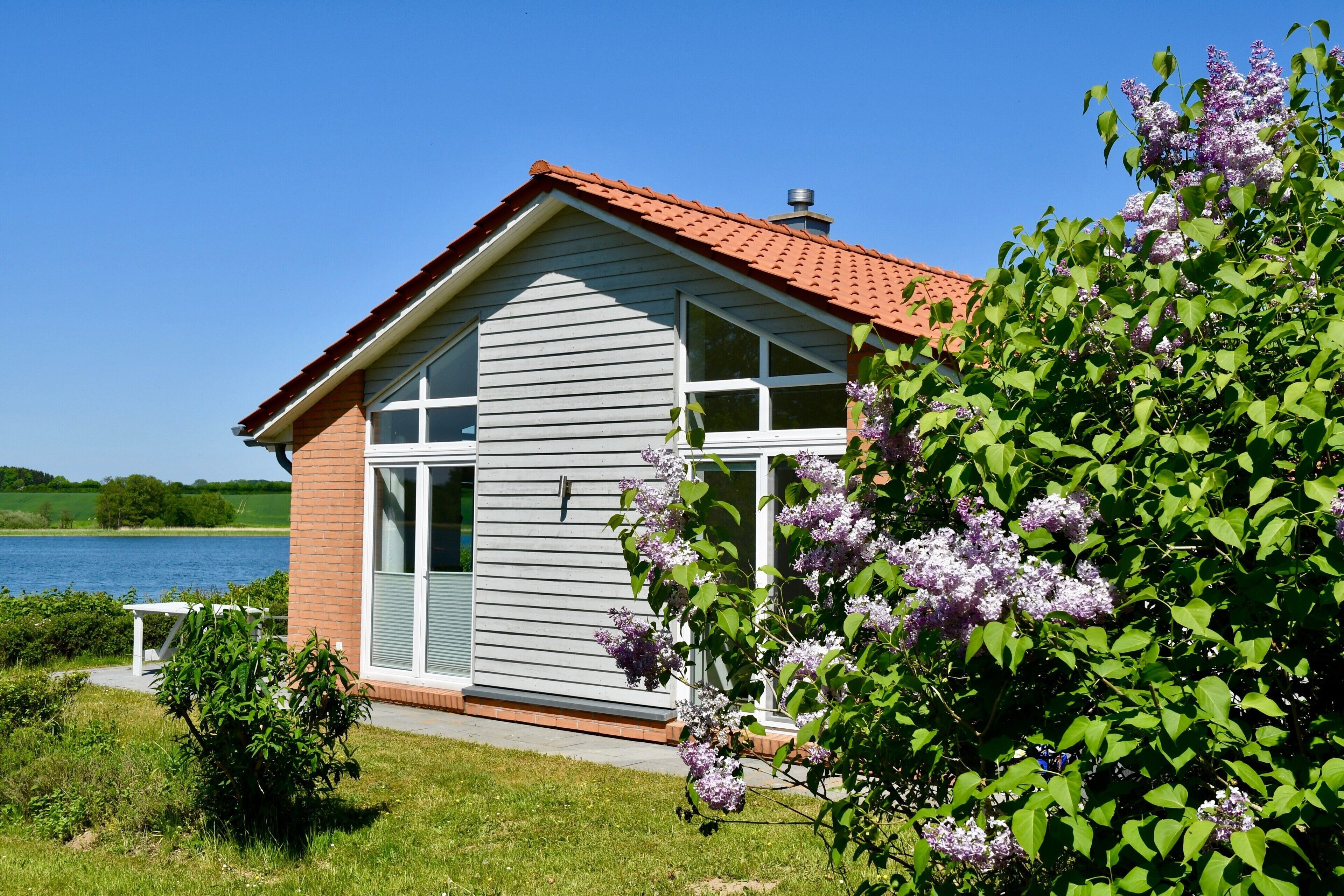 Una casa con techo rojo, ventanas amplias y vista al lago.