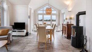 A modern living room with a TV, dining table, chairs, and a fireplace. - Holiday Home 'Schwanenuferhaus' with Sea View, Private Terrace and Wi-Fi (Kosel)