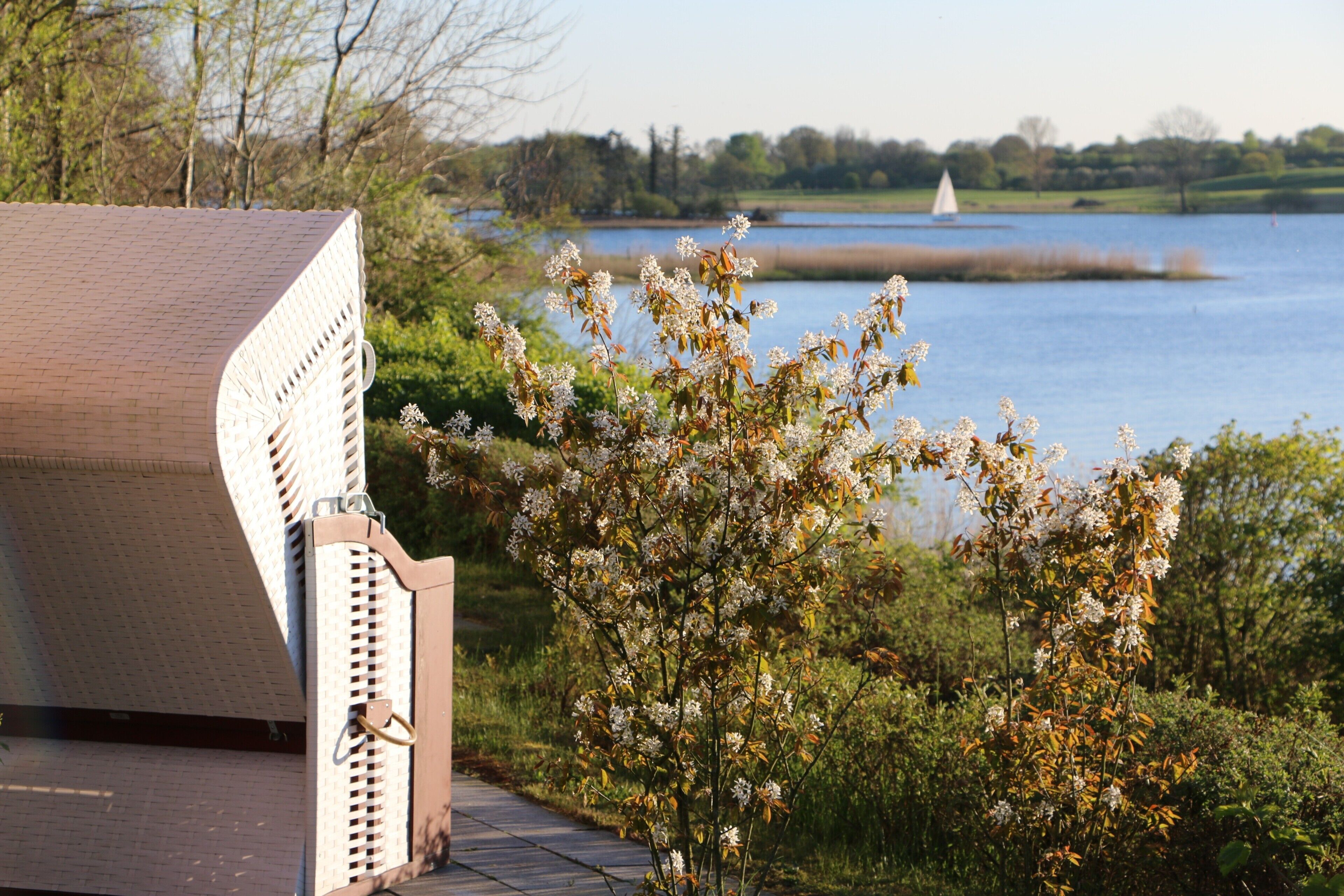 A building with a sloped roof and a lattice structure, overlooking a body of water with a sailboat in the distance.